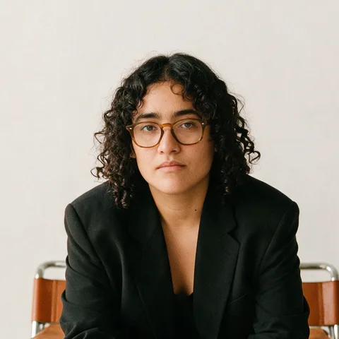 Portrait of Andrea from Tranznora, wearing glasses and a black blazer.